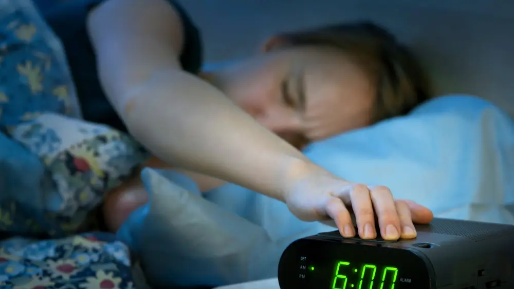 Femme qui a mal dormi et qui éteint son réveil à 6 heures du matin 
